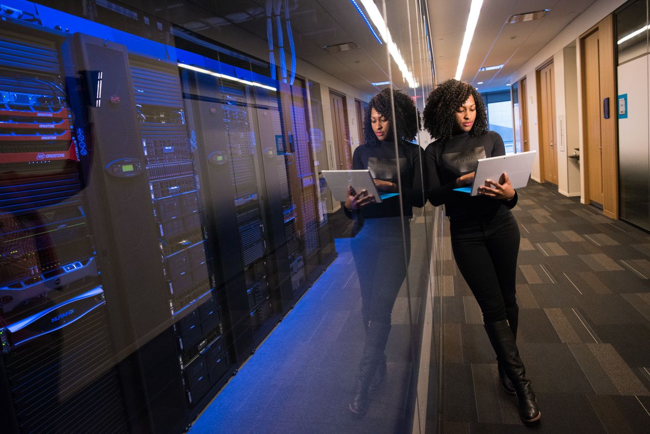 hero-img-01 A woman using a laptop navigating a contemporary data center with mirrored servers.