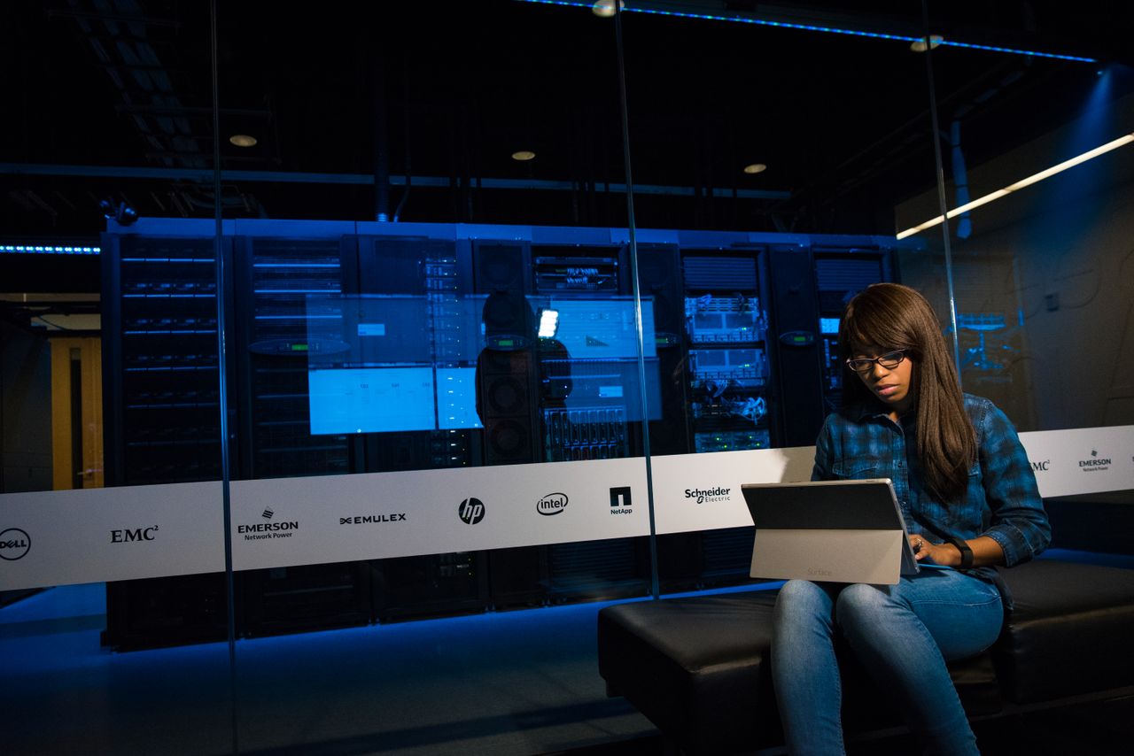 hero-img-02 Woman using a laptop in a server room, showcasing modern technology and work environment.