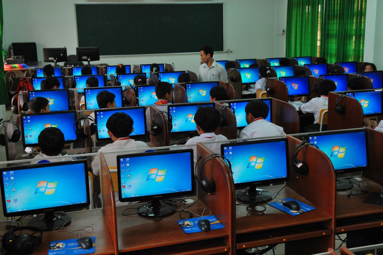 gallery-2 Students learning in a computer lab with multiple monitors and a teacher instructing.