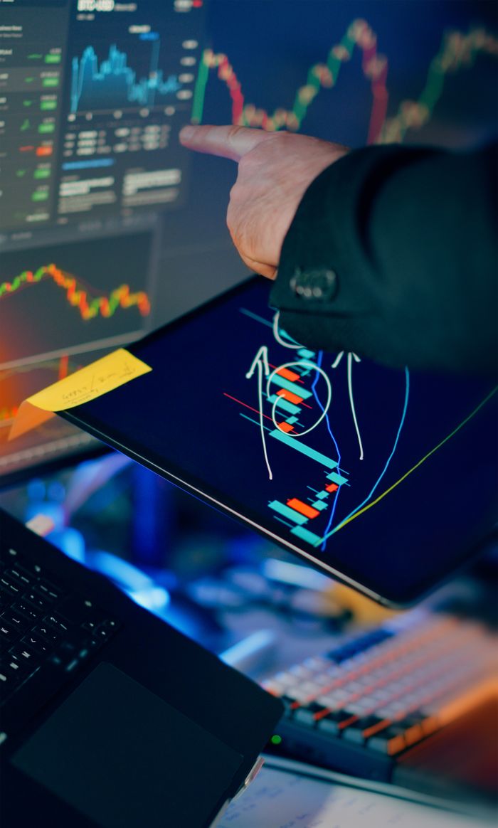 about-01 A business professional examines financial charts on a tablet and monitor for investment strategy.