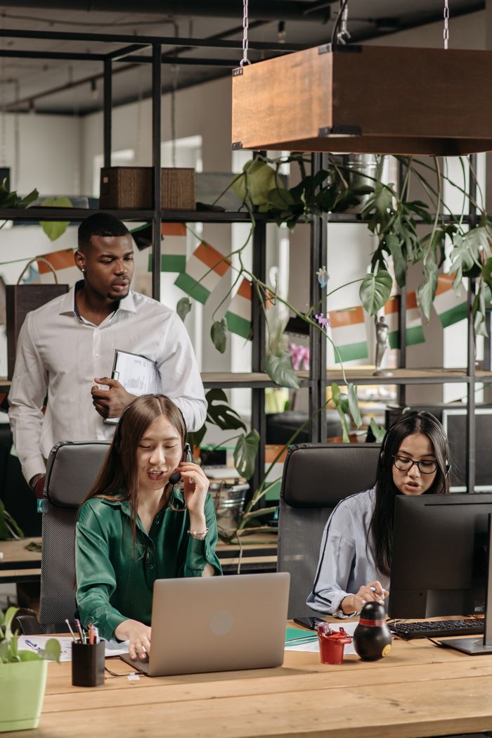 why-choose-us Colleagues in an office setting collaborating on tasks with technology and decor around them.